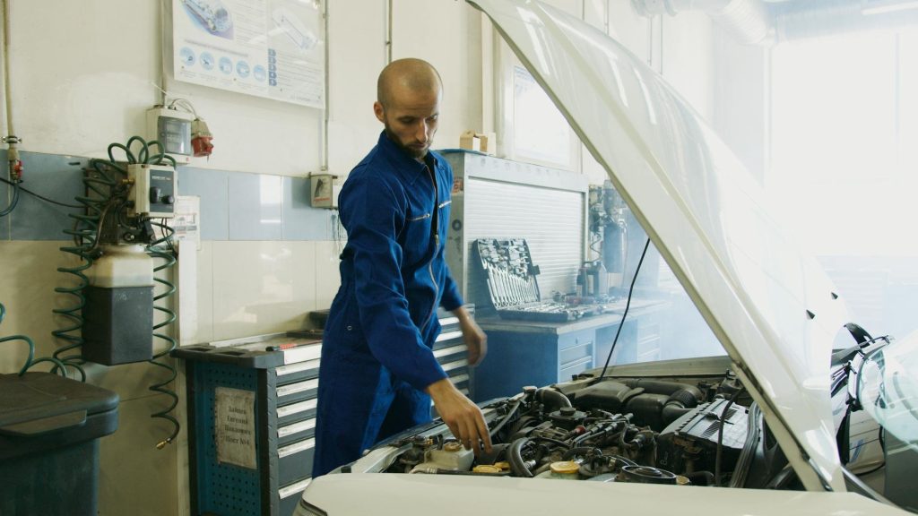 A professional TrustFix Automotive mechanic carefully inspecting a vehicle engine inside a well-lit auto repair garage